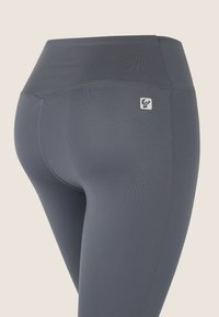 Leggings grises para yoga con cintura alta, textura suave y un pequeño logotipo en la parte trasera. Diseñados para ofrecer flexibilidad y comodidad.