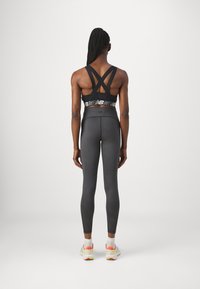 Fekete sportmelltartó, keresztbe rakott pántokkal és logózott szalaggal, sötét szürke, testhez simuló leggings-szel és színes sportcipőkkel párosítva.