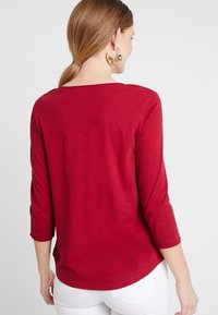 Maglietta borgogna a tre quarti in cotone morbido, con scollatura a girocollo e una superficie liscia e uniforme.