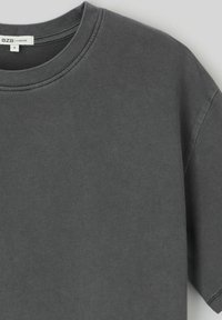 T-shirt surdimensionné à col rond en coton gris foncé. Présente une texture lisse, des manches courtes et des détails de couture visibles sur l'encolure.