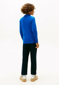 Polo-shirt à manches longues bleu, en coton, associé à un pantalon marine foncé et des baskets. Dispense de poignets côtelés et d'un col classique.