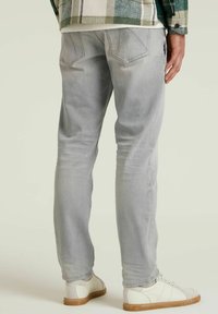 Vaqueros de mezclilla de color gris claro con un ajuste slim, que cuentan con bolsillos traseros y detalles de costura mínimos. Combinados con zapatillas blancas y una camisa de cuadros.