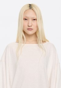 Jasnoróżowy, oversize sweter o luźnym kroju, z dekoltem łódź i miękką teksturą materiału. Minimalistyczny design z opuszczonymi ramionami i subtelnymi szwami.