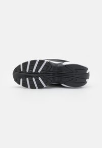 Black athletic shoe sole with textured rubber and traction patterns; features white accents and a distinct multi-directional tread design.