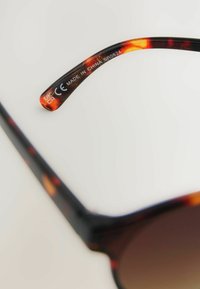 Occhiali da sole tartarugati con finitura lucida e testurizzata. Include la scritta "Made in China". Lenti a gradiente marrone.