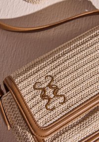 Beige geflochtene Handtasche mit strukturiertem Muster, hellbraunen Lederakzenten, einem gesteppten Rand und einem goldenen gestickten Logo-Detail.
