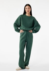 Grøn sweatshirt med overdimenderede ærmer og ribbet halsudskæring, parret med matchende brede sweatpants. Begge lavet af blødt, tekstureret materiale.