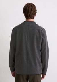 Donkergrijze jas met een gestructureerde kraag, lange mouwen en een nette achternaad. De stof oogt glad met een lichte textuur.