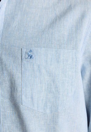 Hellblau und weiß gestreifte Hemdtasche mit kleinem, blau besticktem Hasen nahe der oberen linken Ecke.