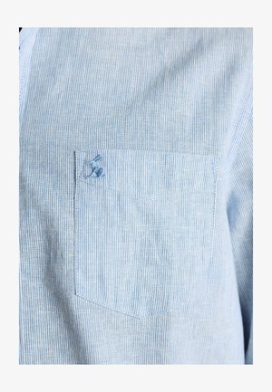 Hellblau und weiß gestreifte Hemdtasche mit kleinem, blau besticktem Hasen nahe der oberen linken Ecke.