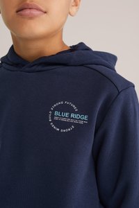 Námořnický modrý mikina z měkké látky s kruhovou grafikou na hrudi, která zobrazuje text "BLUE RIDGE". Minimalistický design, volný střih.