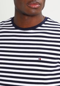 Camiseta de algodón con mezcla en rayas navy y blanca, de manga corta, con cuello redondo y un pequeño logo en el lado izquierdo del pecho.