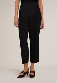 Zwarte op maat gemaakte broek met een hoge taille, twee zijzakken en opgerichte manchetten. Voorzien van twee decoratieve bronzen knopen in de taille.