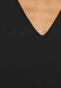 Haut noir à col en V mettant en avant une coupe ajustée et un tissu tricoté texturé, soulignant une construction nette et sans couture au niveau du col.
