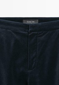 Pantalon en velours bleu foncé avec une fermeture éclair cachée à l'avant et une étiquette « Massimo Dutti » à l'intérieur de la ceinture.