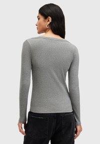 Top grigio a maniche lunghe in texture a costine, con scollatura ampia e design aderente, abbinato a pantaloni neri a vita alta.