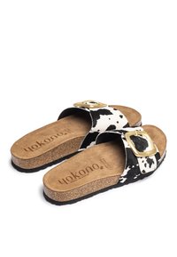 Cowhide slippers met een zwart-wit gevlekt patroon, voorzien van een gouden gesp, kurken voetbed en een gestructureerde zwarte rubberen zool.