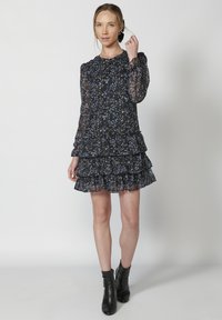 Rochie neagră cu flori, cu mâneci lungi din material transparent, volane și decolteu rotund. Prezintă un model floral albastru și alb pe un material ușor.