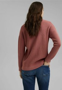 Pull en maille rose, à la coupe décontractée, avec un motif texturé et des poignets côtelés, associé à un jean en denim bleu. Pas de logos ni de motifs visibles.