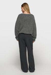 Übergroßer grauer Pullover mit einer weichen, flauschigen Textur, kombiniert mit locker sitzenden dunkelgrauen Hosen. Der Pullover hat weite Ärmel und einen leicht verkürzten Saum.