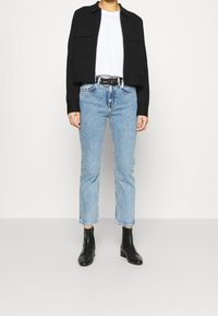 Veste noire courte avec deux poches avant, associée à un jean droit bleu clair et des bottines noires. T-shirt blanc simple en dessous.