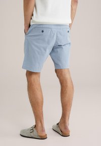 Hellblaue Cordshorts mit lockerer Passform, ausgestattet mit zwei Rückentaschen mit Knopfverschluss und Seitentaschen. Getragen mit grauen Slippers.