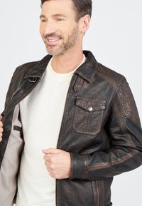 Braune Lederjacke mit Reißverschluss, Druckknopf-Taschen und strukturierten Schulterakzenten. Die Innenseite verfügt über ein leichtes Futter und eine Innentasche.