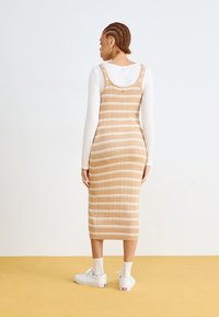 Tan ribbet midi-kjole med hvite striper, justerbare stropper og en tettsittende design, kombinert med hvite sneakers og ankelstrømper.