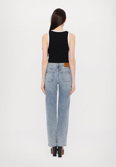 Musthave must sõna musta värvi tank top valge äärisega, millele on kombineeritud helesinised kõrge vöökohaga sirged teksad. Seljal on näha õmblus detaile ja bränditud nahkplekk.