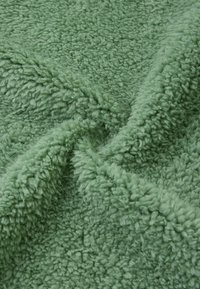 Tessuto verde e morbido con una superficie testurizzata e pelosa, che mette in evidenza una sensazione di morbidezza e comfort. Il materiale sembra spesso e caldo, ideale per coperte.