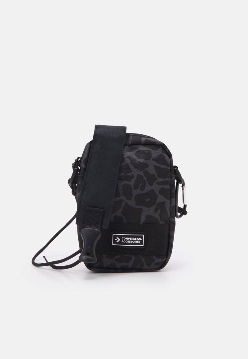 Sac bandoulière à imprimé léopard noir avec fermeture éclair, bandoulière réglable et écusson logo. Fabriqué en tissu durable avec une texture lisse.