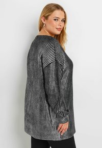 Langärmliges Oberteil in Schwarz mit silbernen metallischen Streifen. Hat eine lockere Passform, gerippte Bündchen und einen leicht abgerundeten Halsauschnitt. Weiche Textur.