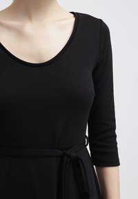 Robe noire en tissu doux, dotée d'un décolleté rond, de manches trois-quarts et d'une ceinture à la taille pour un ajustement réglable.