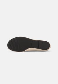 Σόλα ενός μπεζ επίπεδου παπουτσιού με μαύρη υφή από καουτσούκ στη σόλα και τη φτέρνα, εμφανίζοντας το μέγεθος 37 και το όνομα της μάρκας στη μεσαία σόλα.