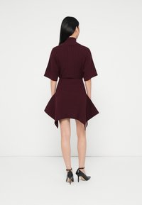 Burgundi színű, bordás ruha gallérral, rövid ujjakkal és bővülő szegéllyel. A lábbeli fekete magassarkú cipő, bokapánttal.