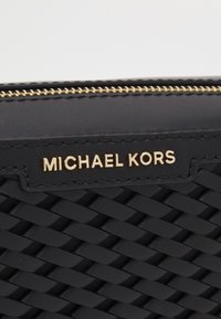 Cartera de cuero trenzado negro con cremallera dorada y logo. Presenta una superficie texturizada y forma rectangular plana para un diseño compacto.