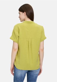 Korte mouwen, lichtgroene blouse met een kraag, voorzien van een rugplooitje en een soepele textuur. Gegdragen met casual blauwe jeans.