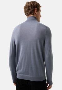 Pull en tricot bleu clair avec un col haut, des poignets côtelés et un ourlet côtelé. Texture lisse, design ajusté et détails de couture minimaux.