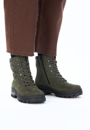 Green suede ankle boots with lace-up design, grey fur accents, and a side zipper. Thick black rubber sole with tread for grip.