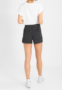 Shorts negros con un diseño geométrico, que presentan una cintura alta y un ajuste relajado, combinados con botines blancos hasta el tobillo y una camisa blanca con mangas enrolladas.