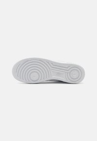 White Nike sneaker outsole featuring circular patterns, rubber material, textured grip, and distinct branding logo in the center.