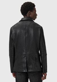 Schwarze Lederjacke mit strukturiertem Finish, schlanker Schnitt, eingekerbtem Kragen und langen Ärmeln; verfügt über eine Stichdetails auf dem Rücken.