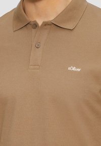 Polo marron en tissu texturé, doté d'un col classique, de deux boutons et d'un petit logo s.Oliver blanc sur la poitrine.