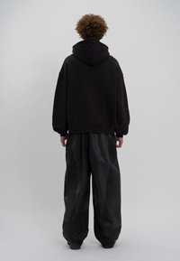 Sweat à capuche noir surdimensionné avec une capuche à cordon, associé à un pantalon large noir en tissu doux et texturé.