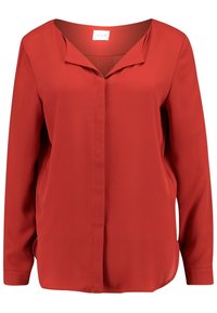 Blouse rouge à manches longues en tissu lisse. Dotée d'un décolleté en V et de détails de coutures verticales à l'avant. Coupe droite avec fentes sur les côtés.