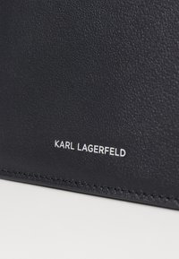Cartera de cuero negro texturizado con el logo en relieve "KARL LAGERFELD" en blanco, con un delicado detalle de costura a lo largo de los bordes.