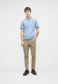 Hellblaues kurzärmeliges Poloshirt mit Kragen und drei Knöpfen, kombiniert mit beigen Chinos und braunen Schnürschuhen. Einfaches Design.