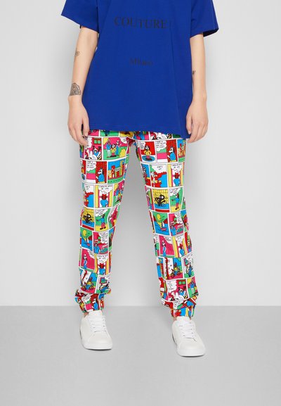 T-shirt azul oversized com o texto "COUTURE ! Milano", combinado com calças de padrão divertido de banda desenhada e sapatilhas brancas.