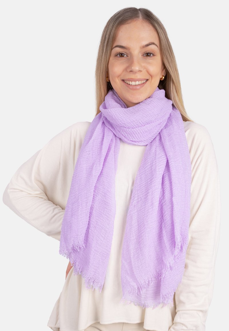 Écharpe lavande en tissu texturé, avec des bords effilochés et un design doux et aérien, drapée autour du cou sur un haut crème.