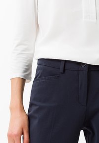 Pantalons marine avec une finition texturée, présentant un devant plat, des poches latérales et des passants de ceinture. Associés à un haut à manches longues blanc.
